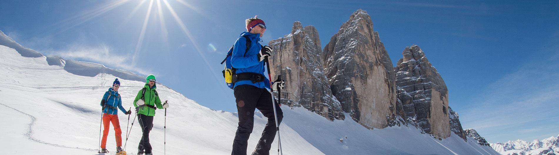 Tre persone che fanno escursione con le ciaspole, con le Tre Cime di Lavaredo sullo sfondo