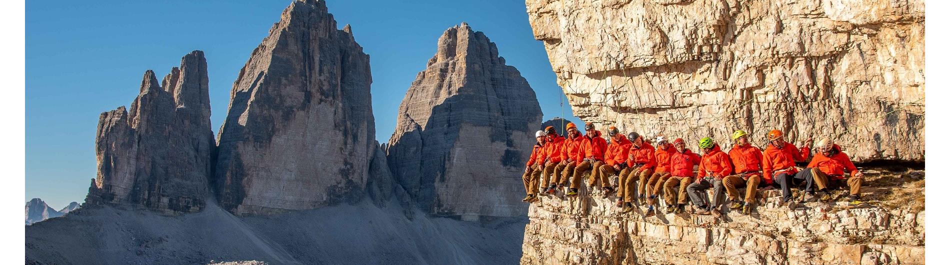 Membri della scuola di alpinismo di Sesto seduti insieme sulla roccia. Sullo sfondo, le Tre Cime di Lavaredo.