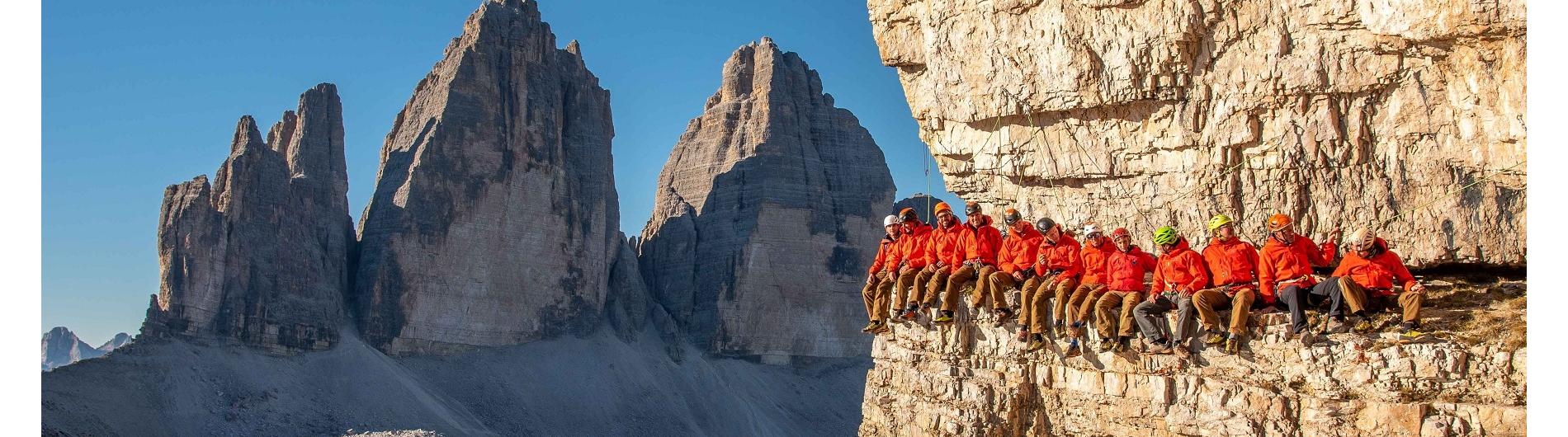 Mitglieder der Alpinschule von Sexten, welche gemeinsam am Felsen Sitzen. Im Hintergrund die Drei Zinnen zu sehen.