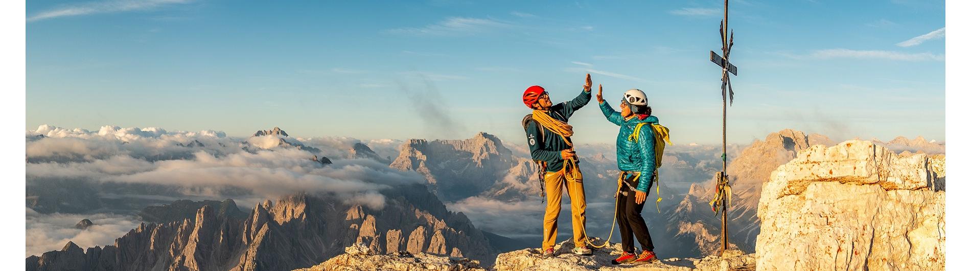Two mountaineers on a summit cross joyfully high-fiving because they have reached their goal.