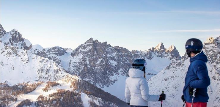 Two skiers seen from behind, watching the peaks of the Tre Cime from the slope